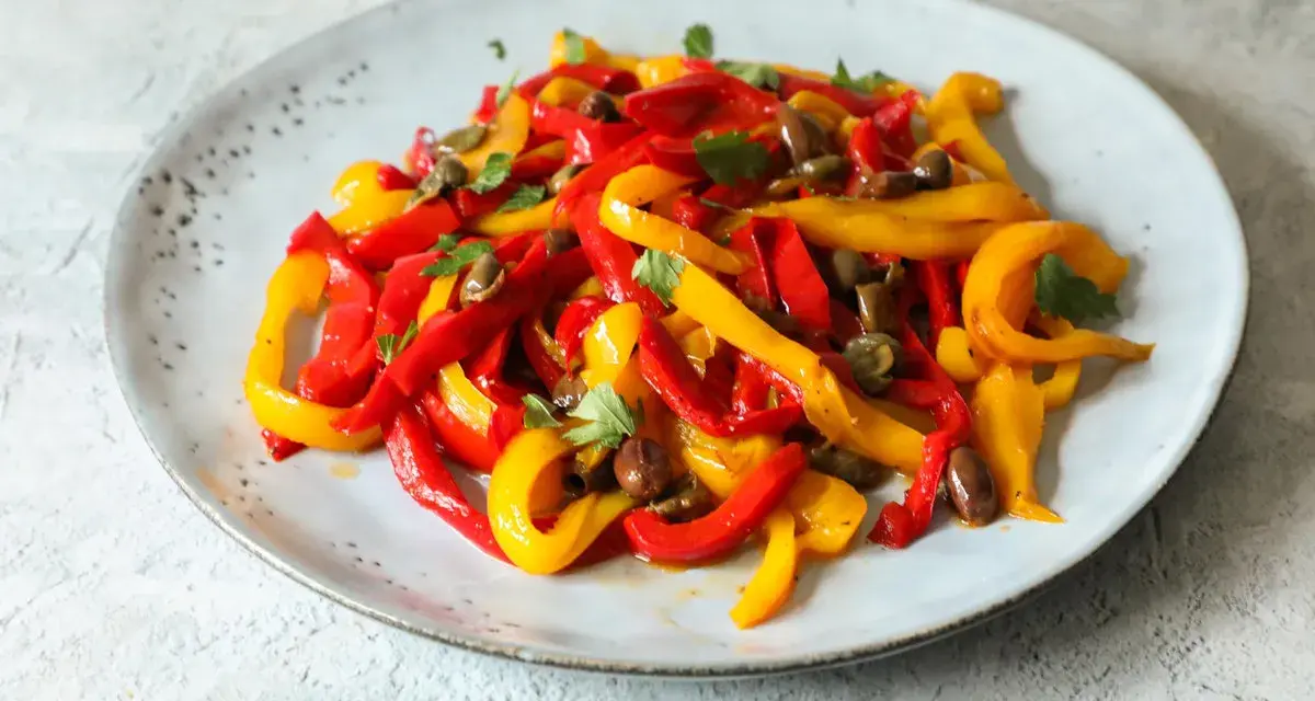 Peperoni in padella, tagliati a listarelle rosse e gialle, conditi con olive e capperi, guarniti con prezzemolo fresco.
