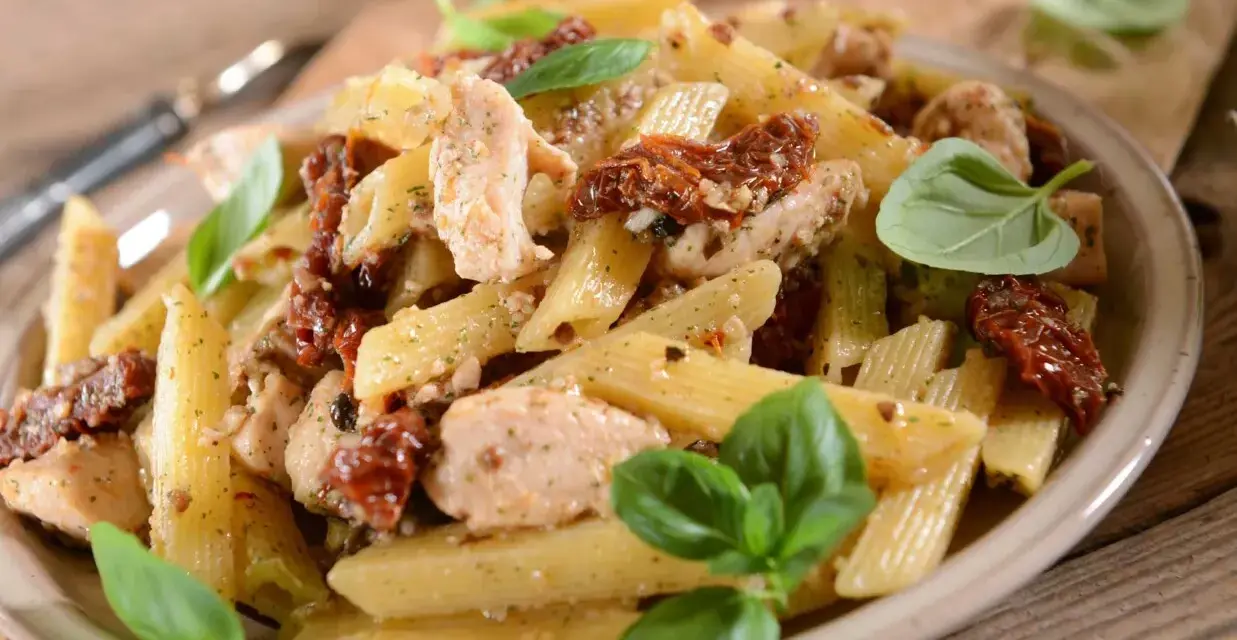 Penne z kurczakiem i suszonymi pomidorami, ozdobione świeżą bazylią. Pyszne danie na obiad.