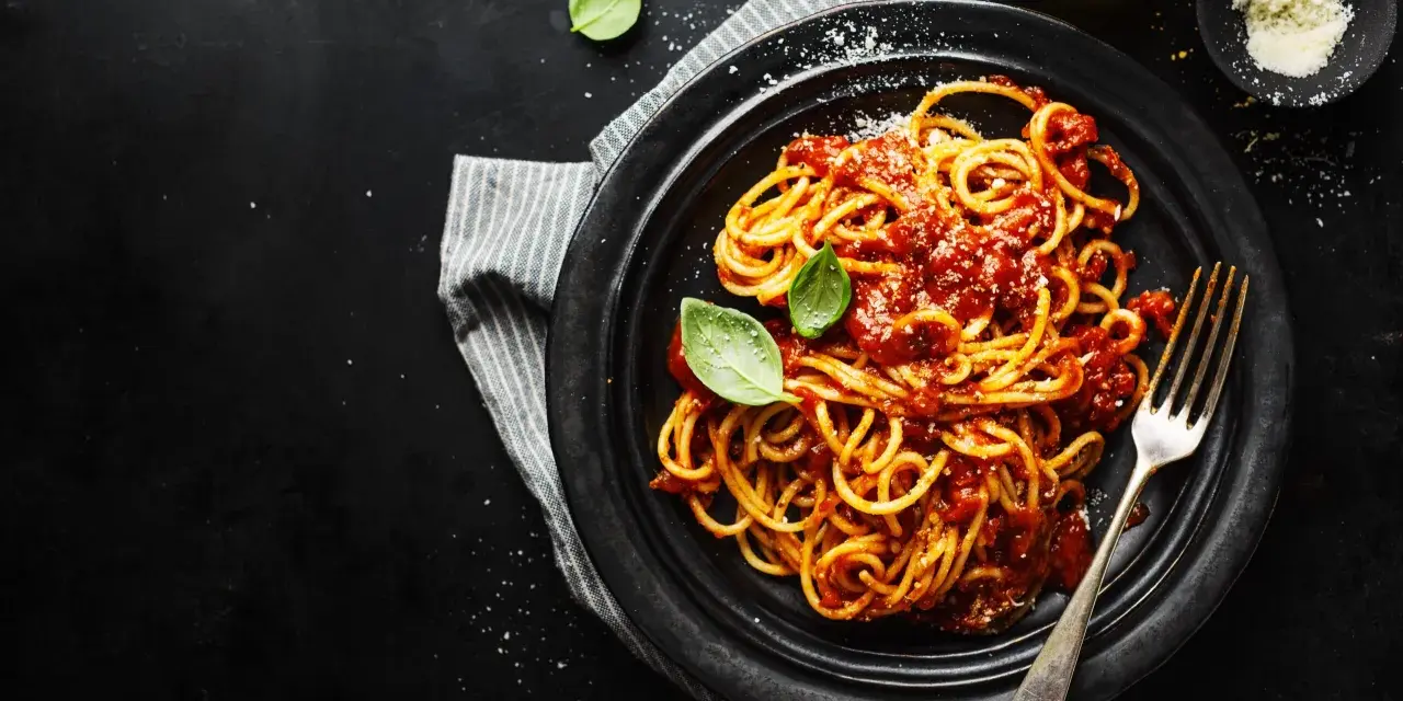 Un piatto di spaghetti alla carrettiera fumanti, conditi con un ricco sugo di pomodoro e basilico fresco, su sfondo scuro.