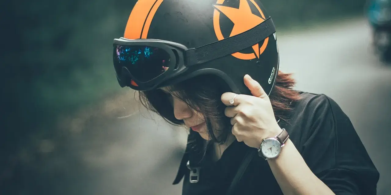 Donna con casco nero e arancione, occhiali riflettenti. Il casco deve calzare bene per la sicurezza.