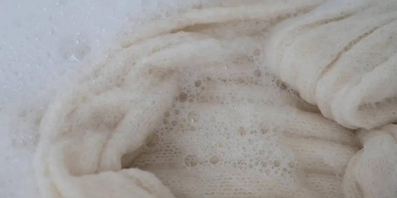 Lana bianca in acqua saponata, un processo che porta all'infeltrimento della lana per creare texture uniche.
