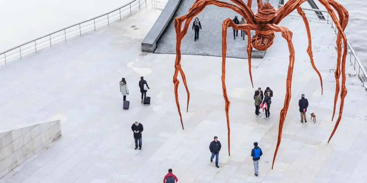 Une immense araignée de bronze, œuvre de Louise Bourgeois, domine une place où quelques passants curieux l'observent.