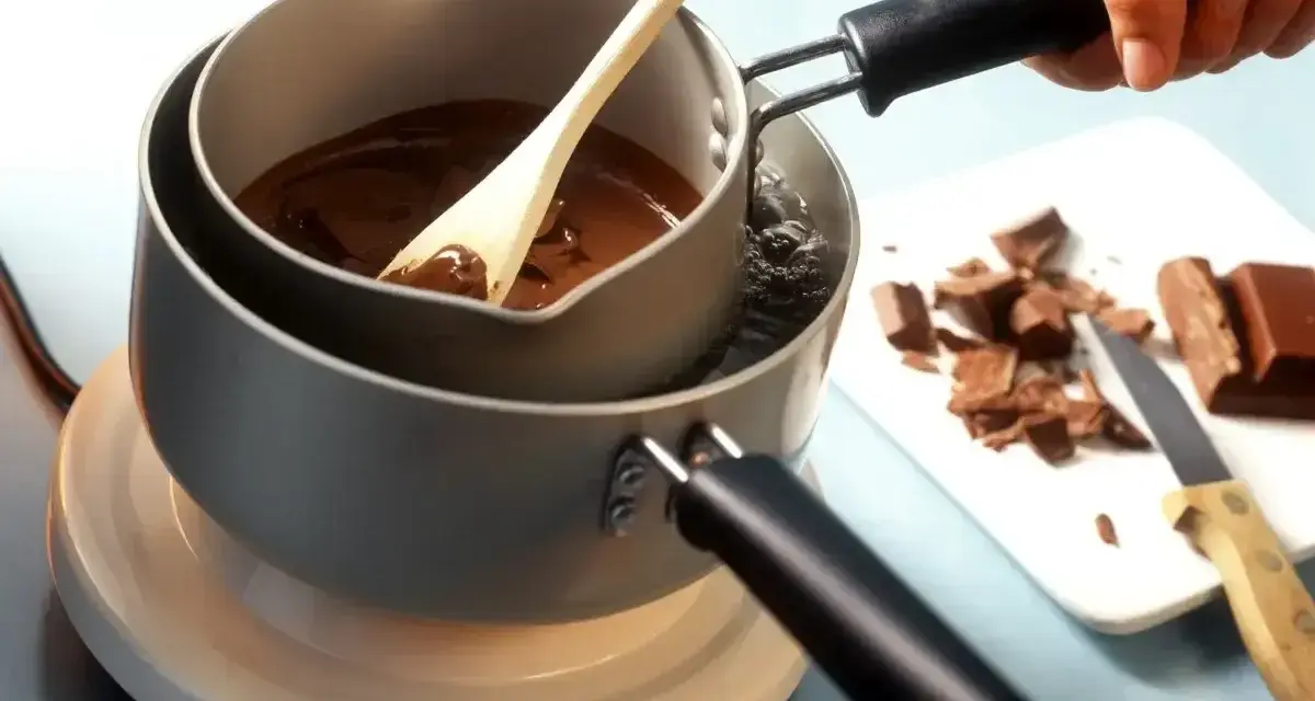 Delikatne topienie czekolady w kąpieli wodnej, by uzyskać idealną konsystencję. Drewniana łyżka miesza płynną masę.