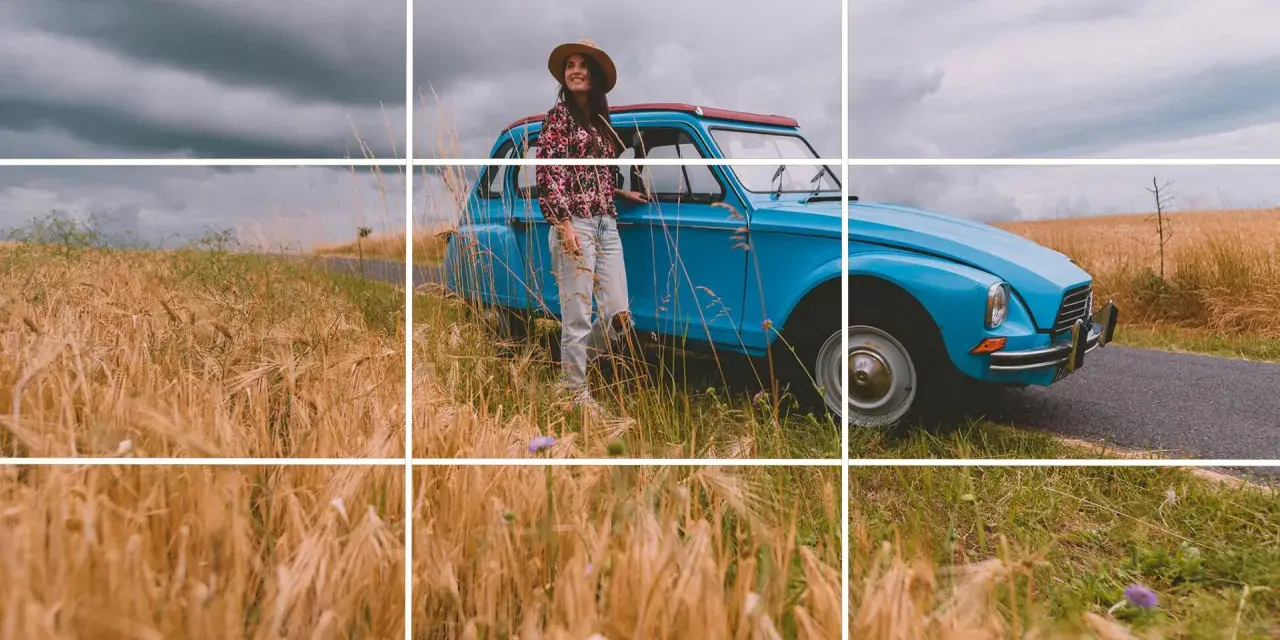 Une femme souriante, chapeau de paille, pose près d'une voiture bleue vintage au milieu d'un champ de blé doré. Photos prises sur le vif.