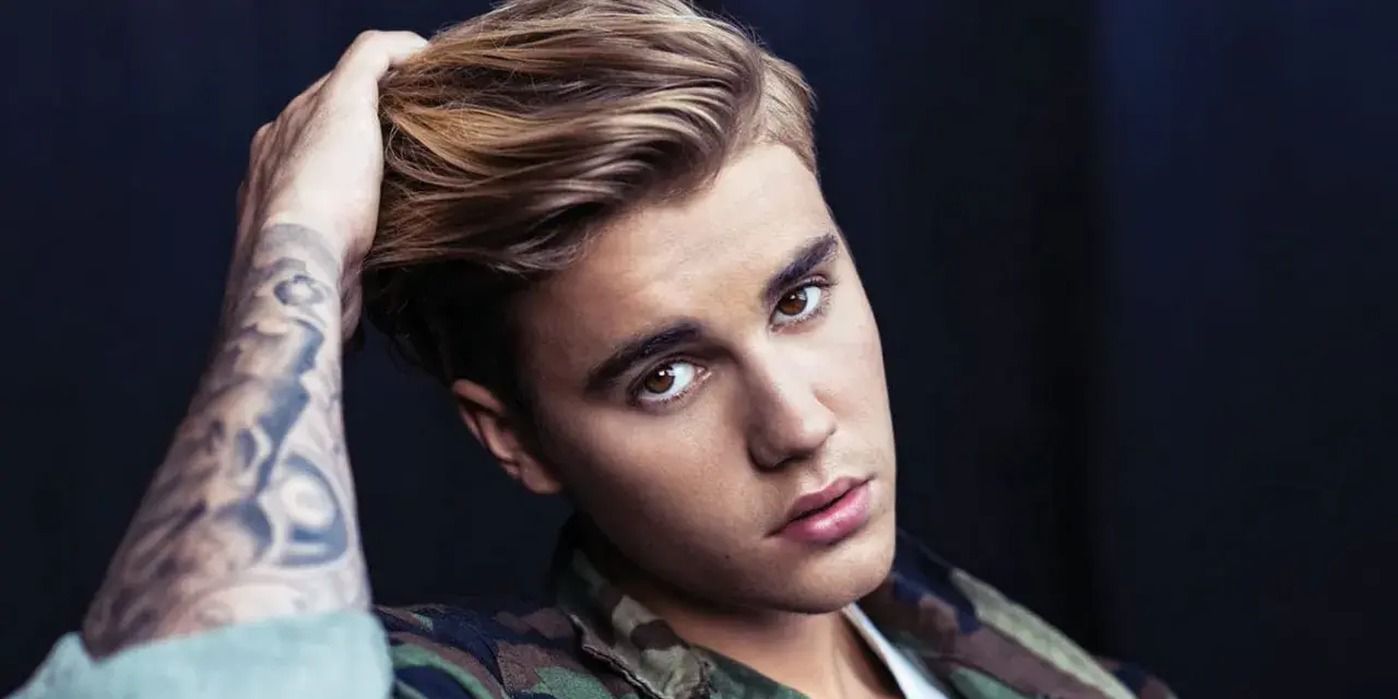 Justin Bieber mit tätowiertem Arm und Camouflage-Jacke, blickt in die Kamera.