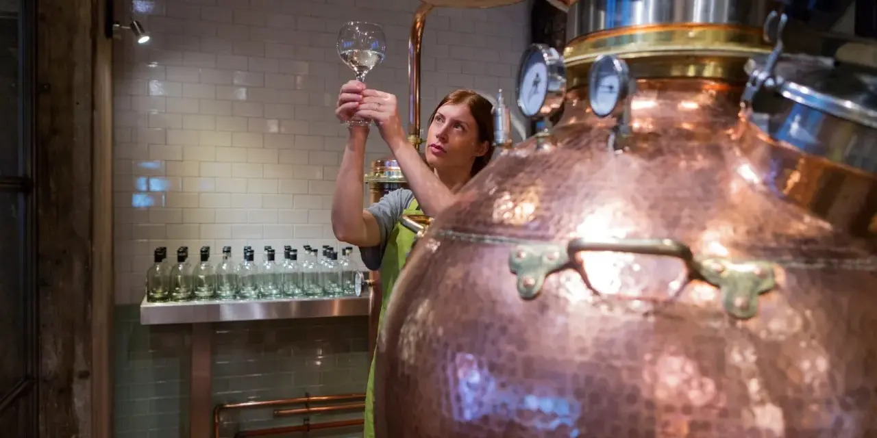 Frau prüft mit einem Glas die Qualität des Destillats. Dies ist ein Schritt, wie wird Gin hergestellt, in einer Kupferbrennerei.