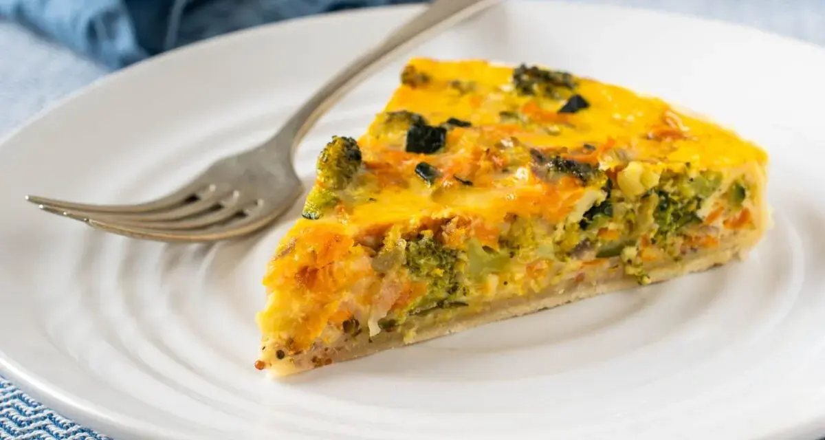 Rebanada de quiche vegetal con brócoli y zanahoria, servida en plato blanco con tenedor.