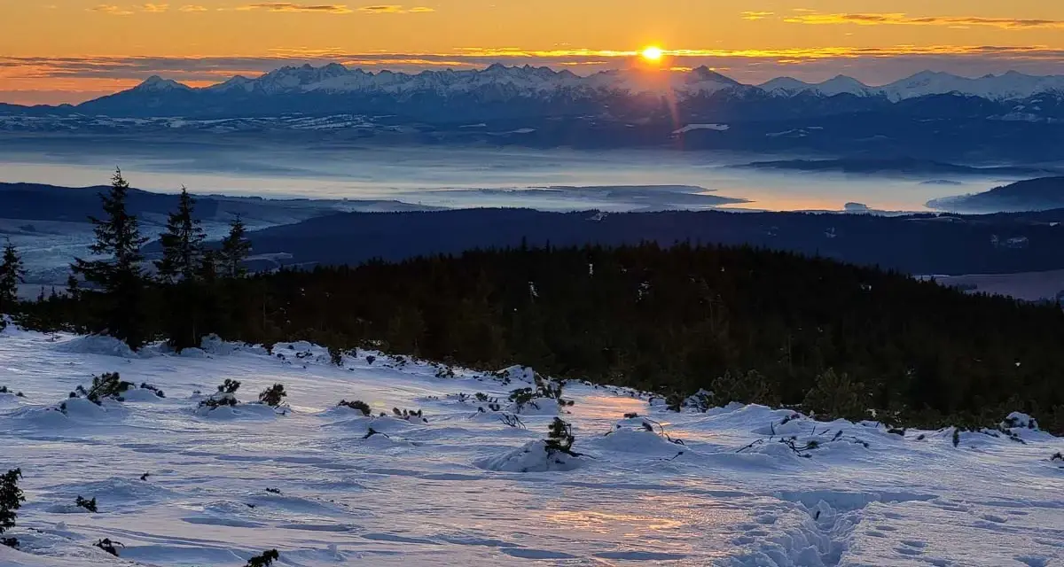 Zachód słońca nad mglistą doliną, ośnieżone szczyty górskie w tle. Odkryj mało znane miejsca na Pomorzu, gdzie zimowy krajobraz zapiera dech w piersiach.