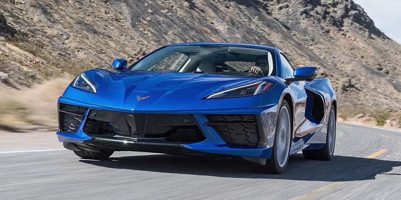 Błękitny Chevrolet Corvette Stingray pędzi po pustynnej drodze.