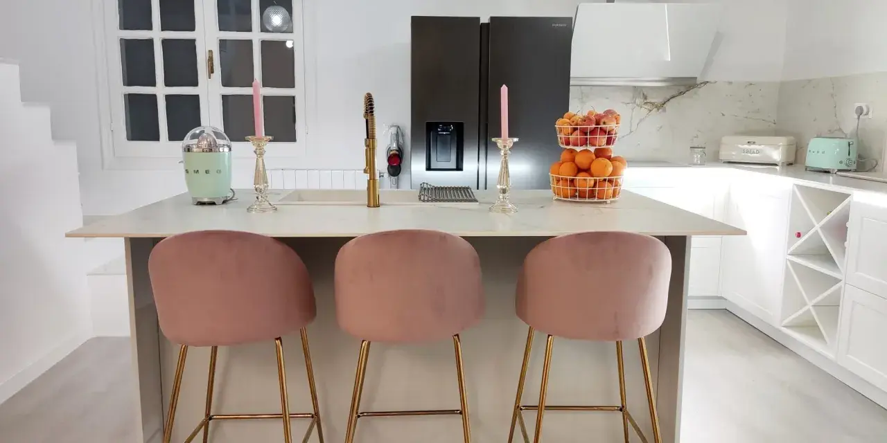 Elegantes cocinas con isla, tres taburetes rosas y dorados invitan a disfrutar.