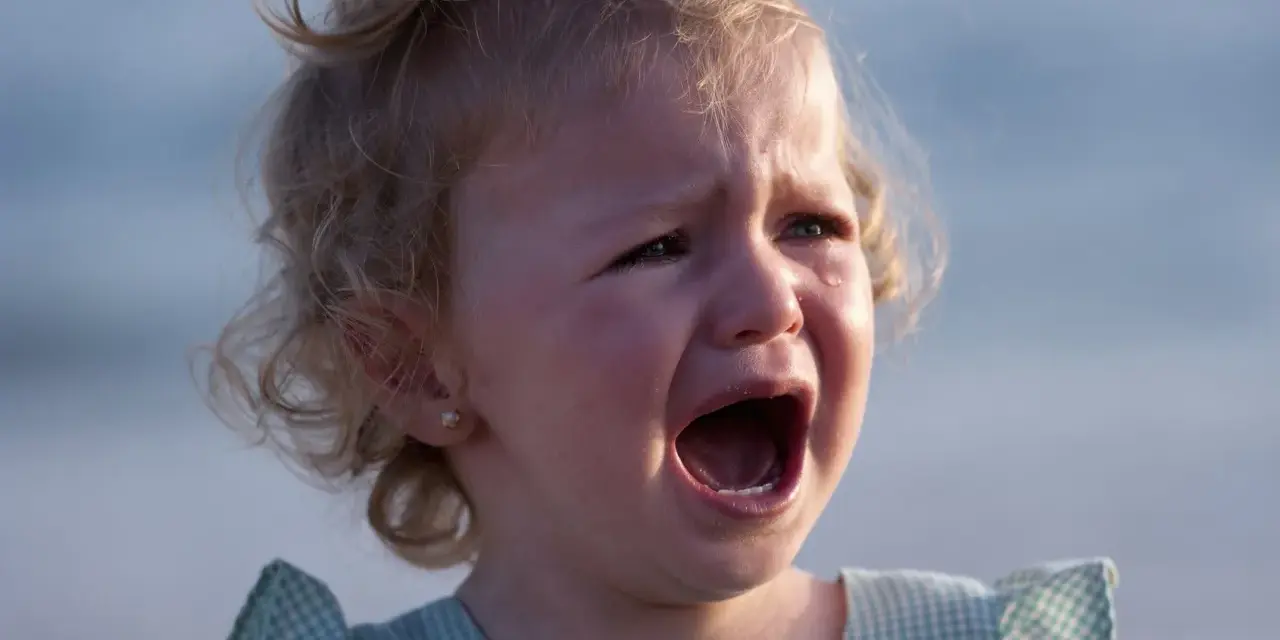 Ein kleines Mädchen mit blonden Locken weint bitterlich. Tränen laufen über ihre Wangen. Wahrscheinlich ist sie mitten in der Trotzphase mit 2 Jahren.