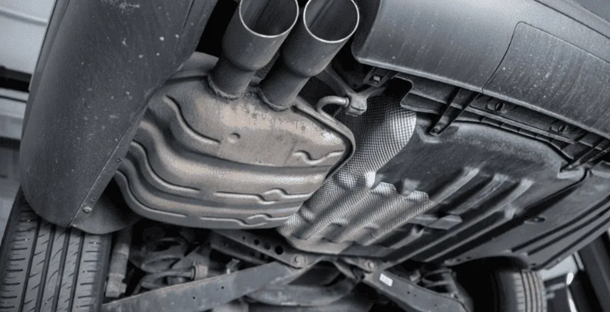 The underside of a car shows a dual exhaust system leading to a large muffler, which is a key component for reducing engine noise.
