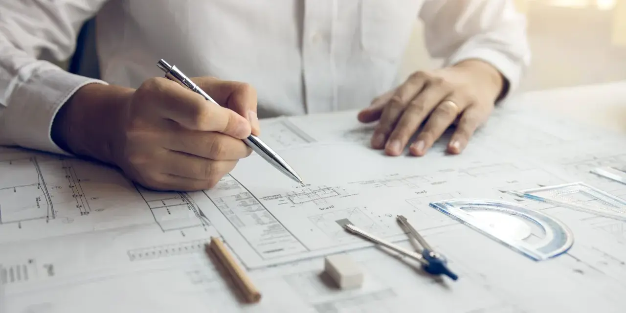 Inżynier z uprawnieniami budowlanymi elektrycznymi analizuje projekt, trzymając długopis nad dokumentacją techniczną.