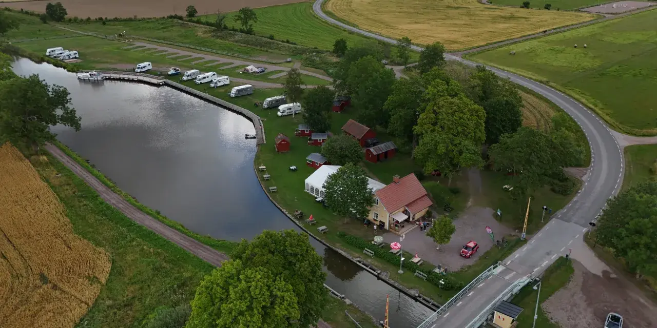 Jonsboda camping vid en kanal med husbilar, båtar och röda stugor. En bro leder över vattnet.