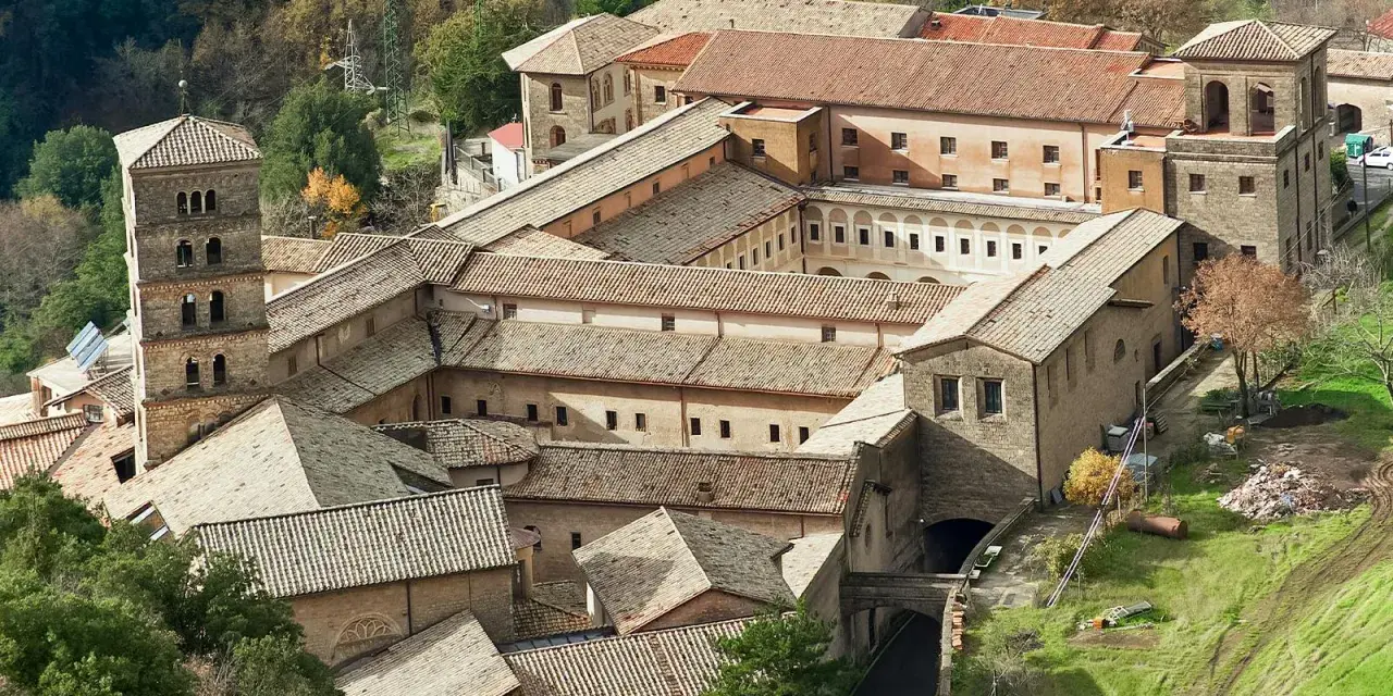 Aerial view of a sprawling monastery complex near Rome, with terracotta roofs and a tall bell tower.