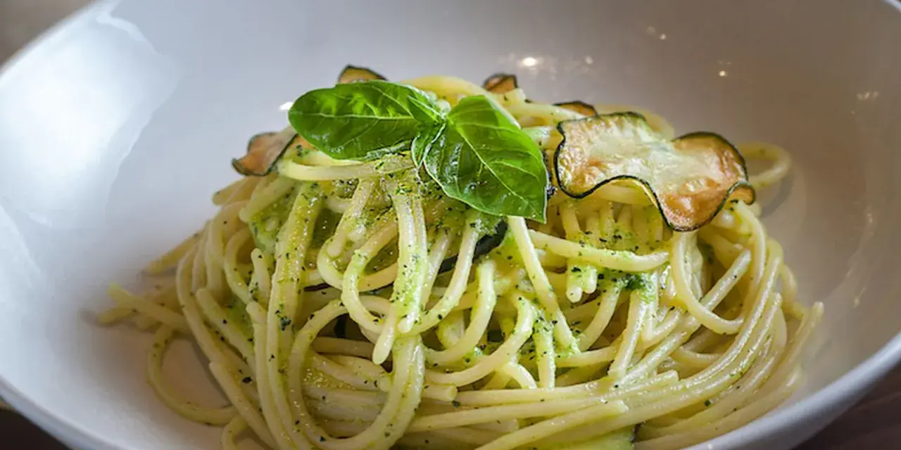 Spaghetti cremosos con calabacín y albahaca en un cuenco blanco.