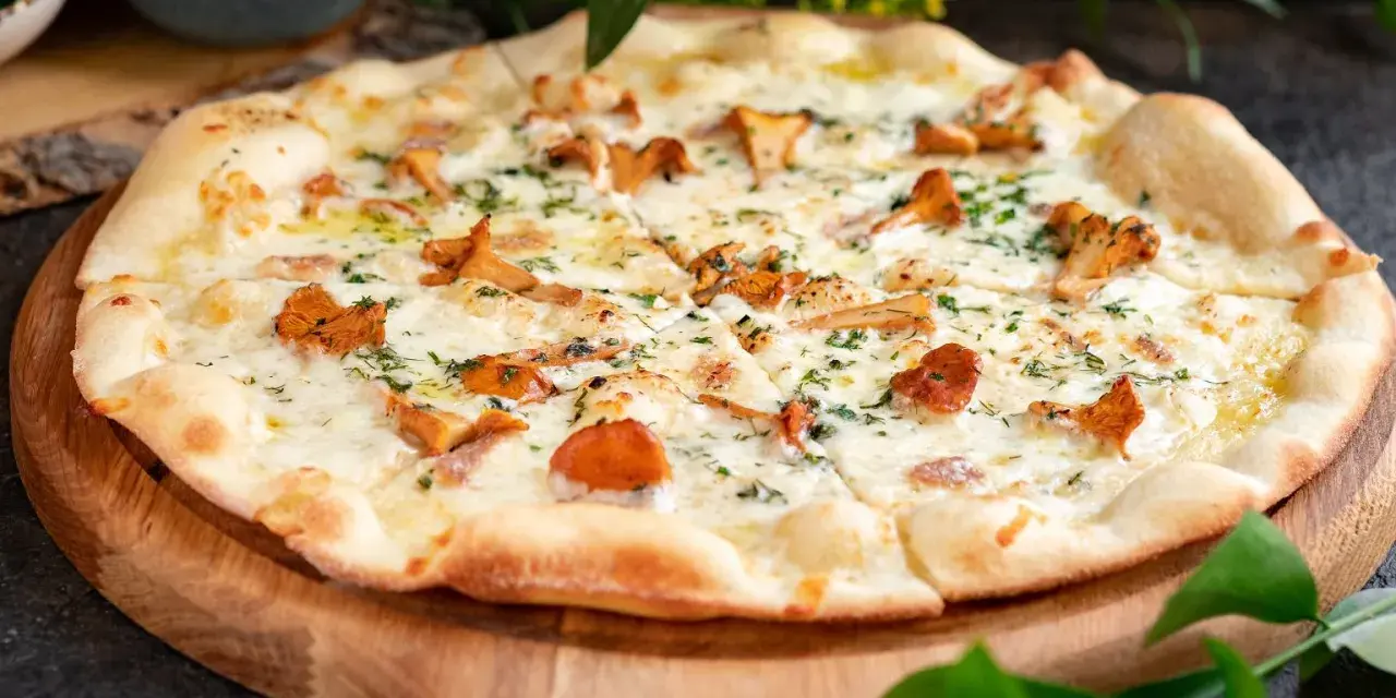 Pyszna pizza z kurkami, polana kremowym sosem i posypana świeżymi ziołami, podana na drewnianej desce.
