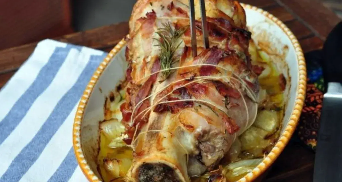 Stinco di vitello al forno, avvolto in pancetta e cotto con cipolle e rosmarino, pronto per essere servito.