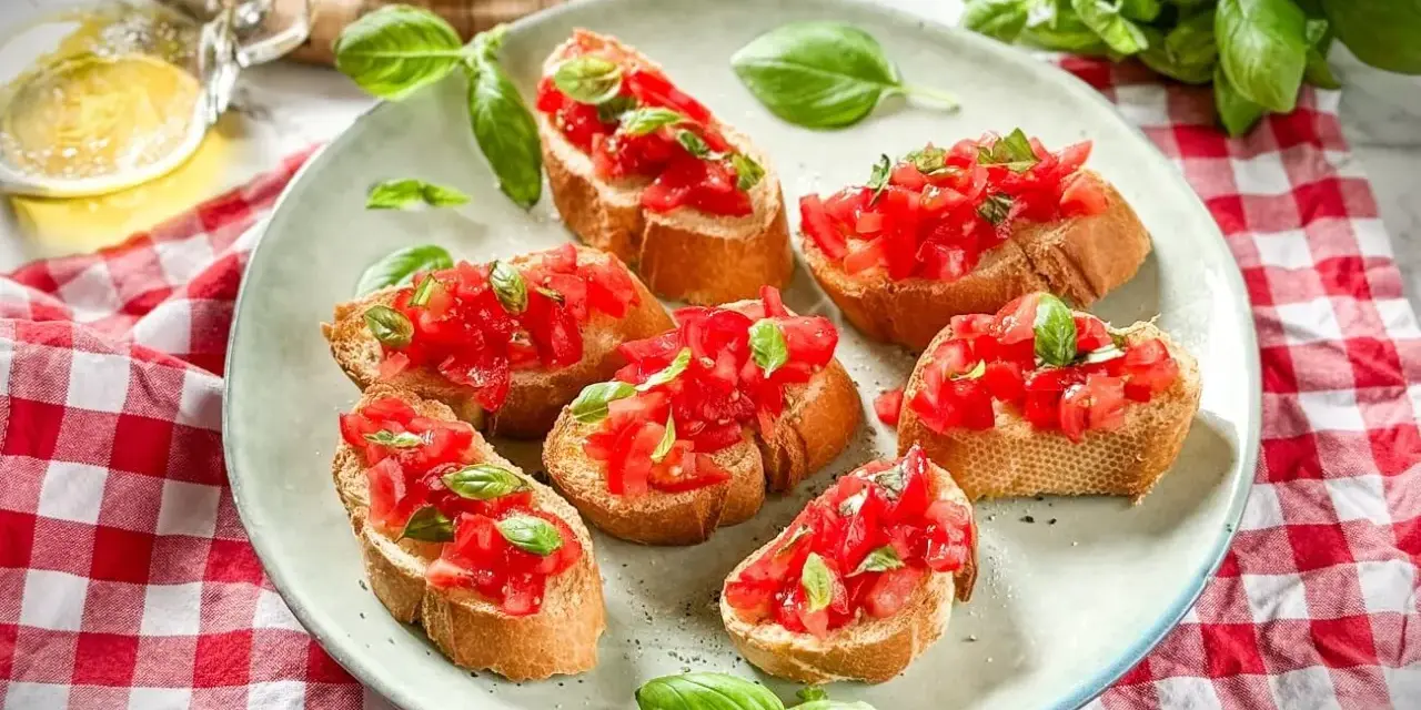 Frische Crostini Variationen mit Tomaten und Basilikum auf einem Teller, garniert mit frischen Basilikumblättern.