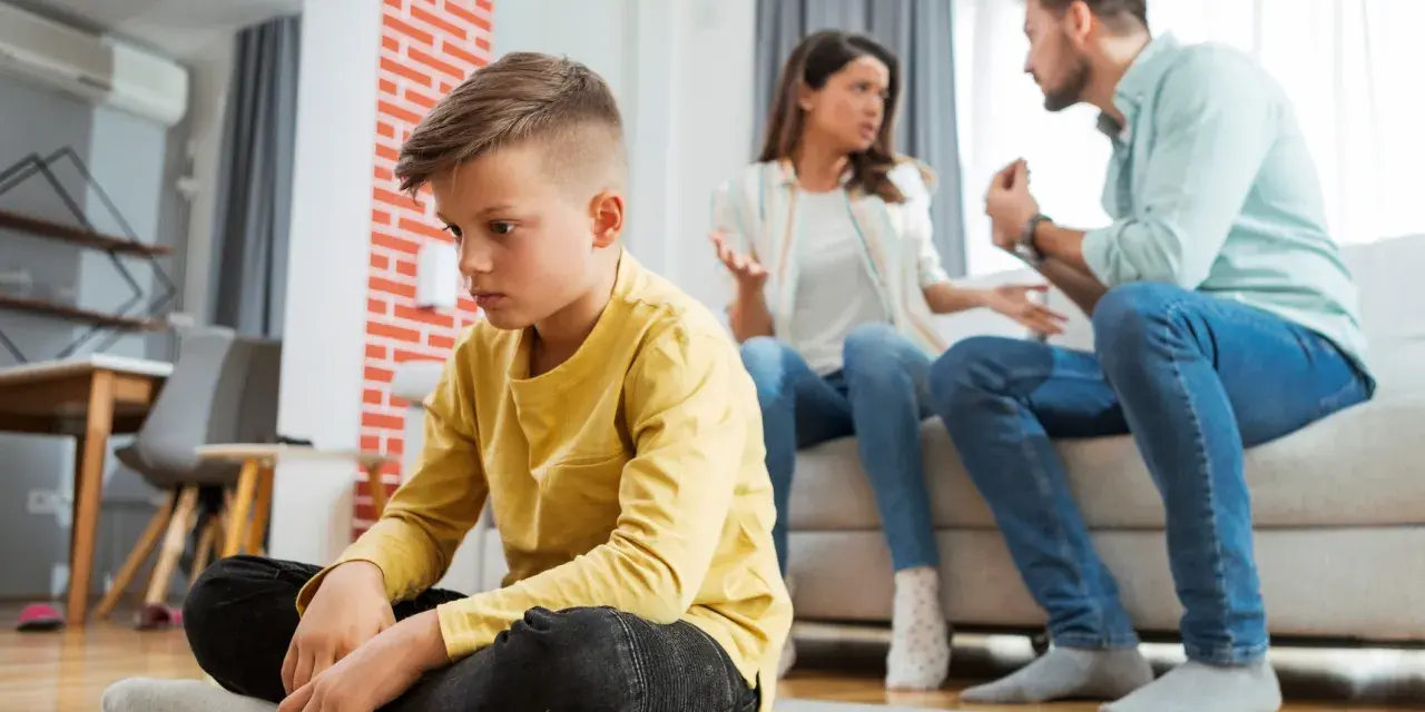 Trauriger Junge sitzt allein, während Eltern streiten. Die Vorteile eines Nebenwohnsitzes für Kinder sind oft, dass sie in einer ruhigeren Umgebung aufwachsen können.