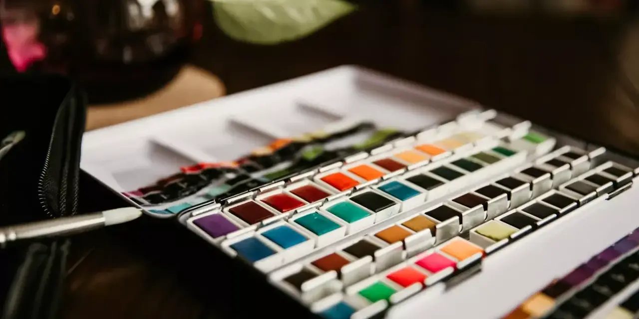 Une palette de matériel peinture aquarelle aux couleurs vives, prête à l'emploi. Un pinceau est posé à côté.