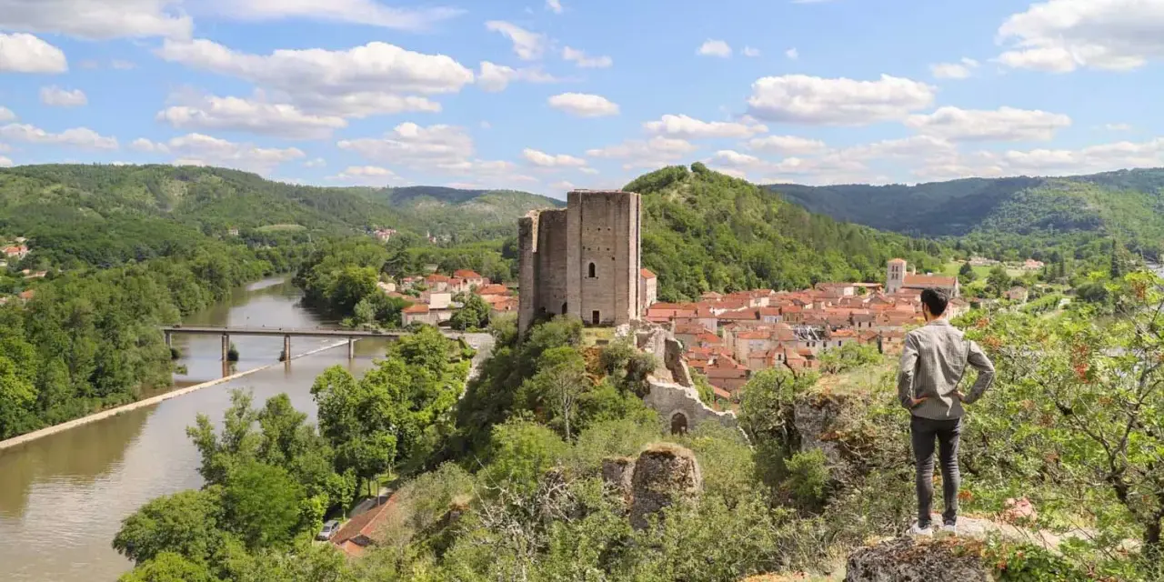 Un homme admire un village médiéval avec un château, un fleuve et des collines verdoyantes, un aperçu du circuit des plus beaux villages du Lot.
