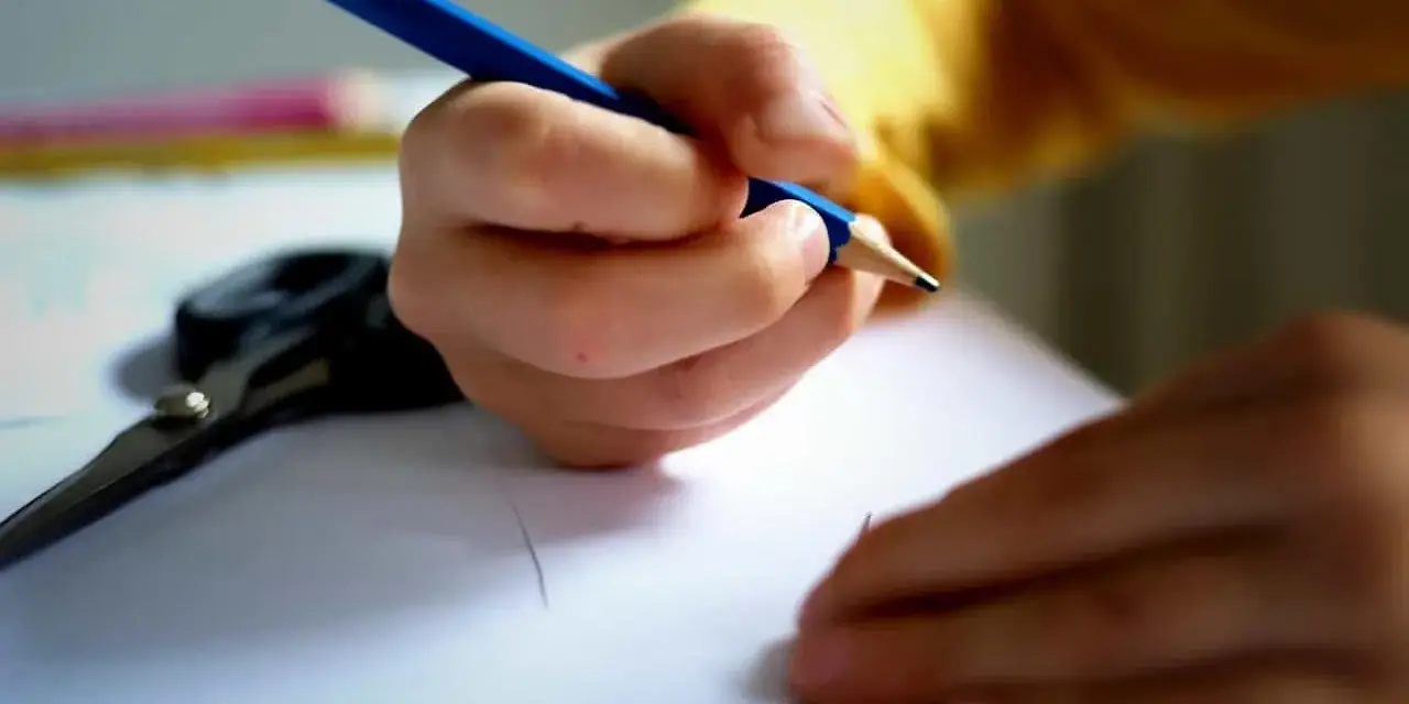 Dziecko pisze wzruszający list do taty. Na stole leżą nożyczki i kredki.
