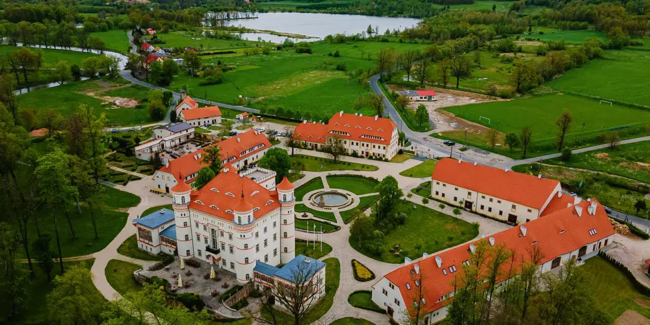 Pałac w Wojanowie otoczony zielenią, z jeziorem w tle. Malowniczy widok z lotu ptaka na zabytkową architekturę i otaczający krajobraz.