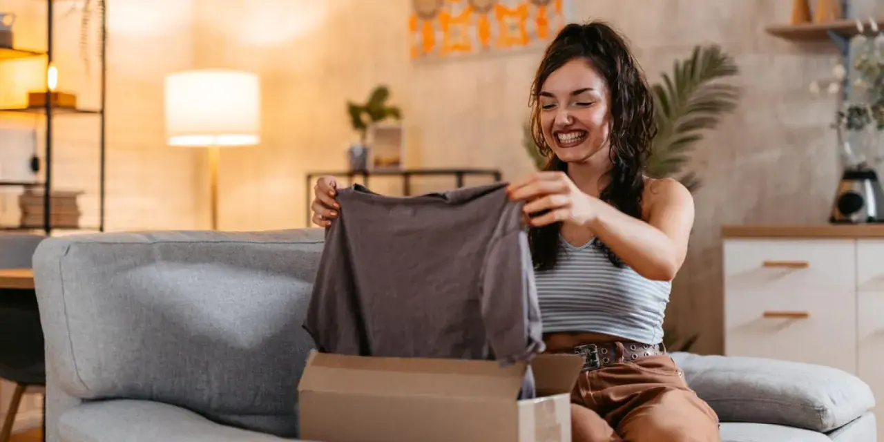 Mujer sonriente desempaqueta una camiseta gris. Espera que las medidas cuerpo sean perfectas.
