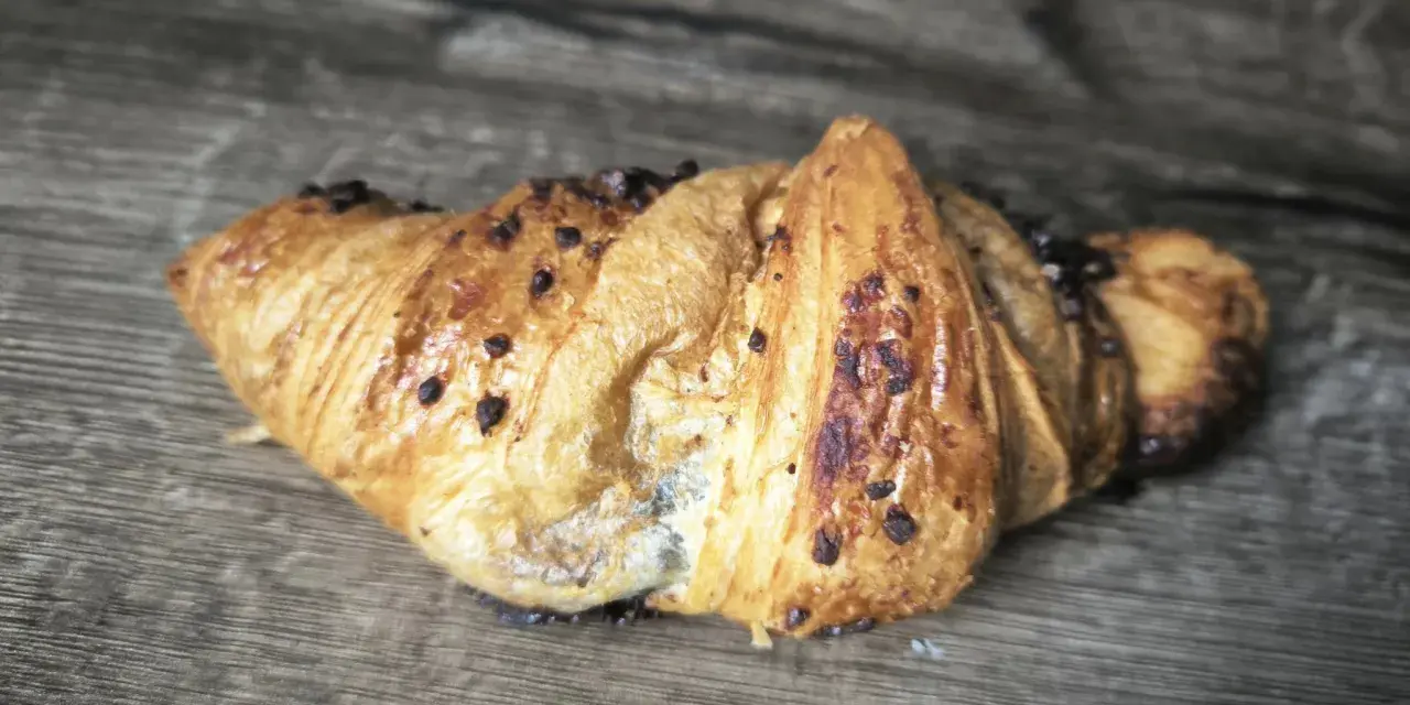 Chrupiący croissant z kawałkami czekolady na drewnianym tle. Idealny na śniadanie, choć warto sprawdzić jego kcal.