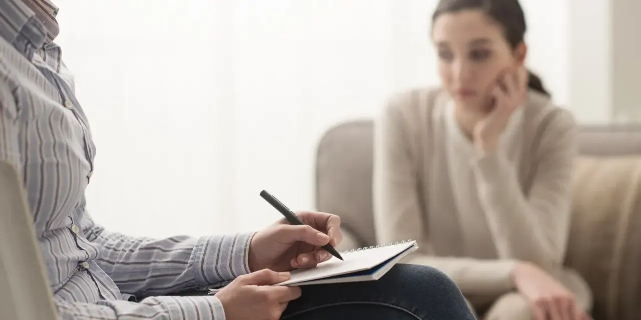 Psycholog notuje, analizując sytuację pacjentki. Zarobki psychologa zależą od doświadczenia i specjalizacji.