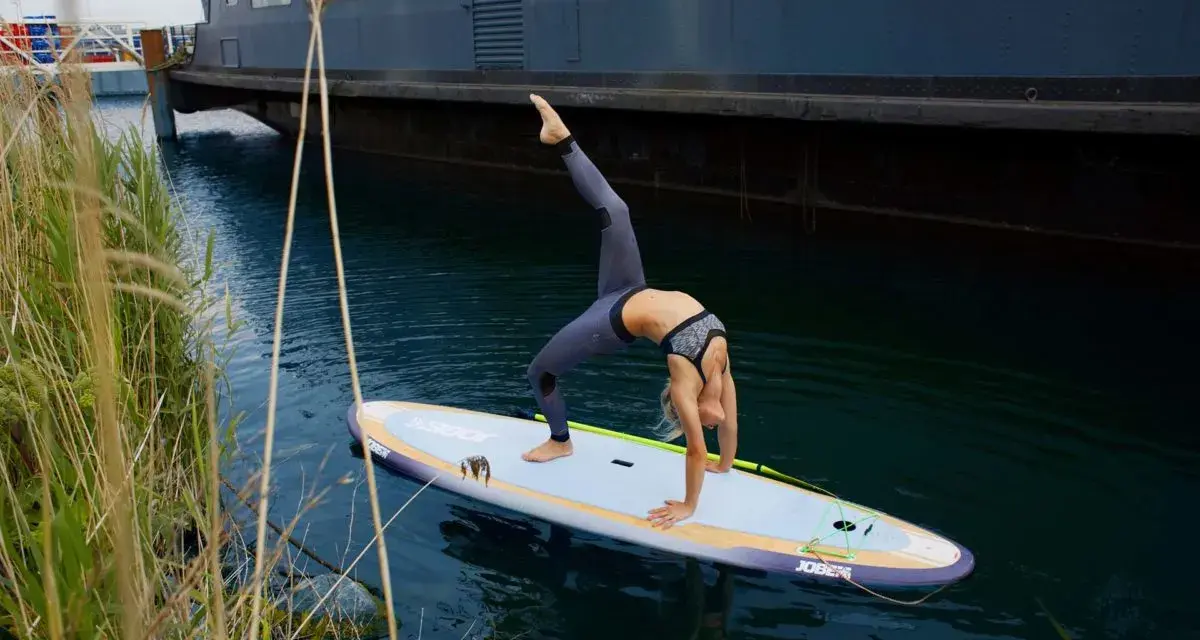 Frau macht Yoga-Brücke auf SUP-Board. Stand up paddle gesund und fördert Balance.