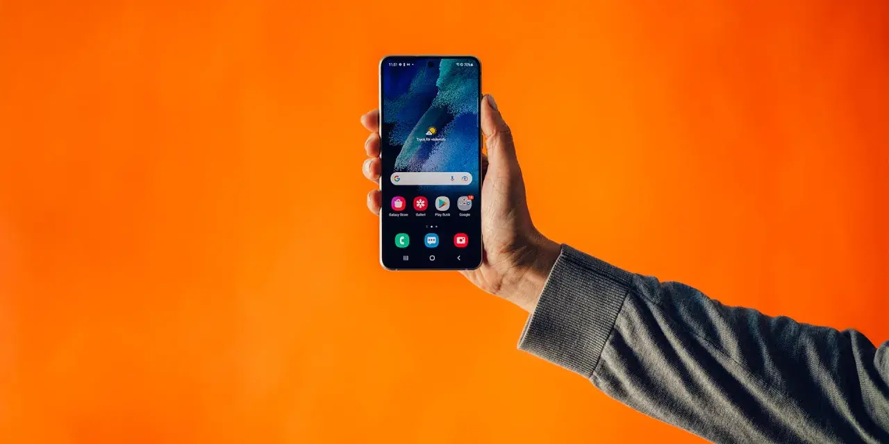 En hand håller upp en smartphone mot en orange bakgrund. Kanske en lösning på problem med dubbla simkort?