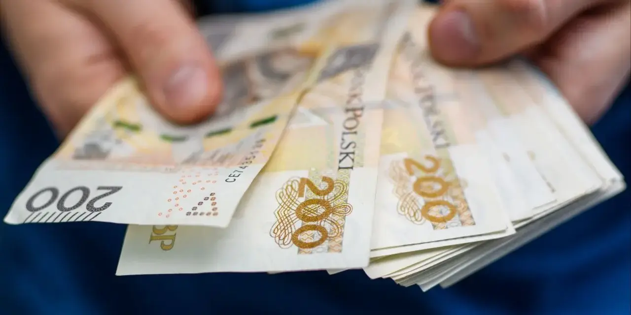 Dłonie trzymające stos banknotów 200 zł. Może to symbolizować zarobki w najlepiej płatnych zawodach.