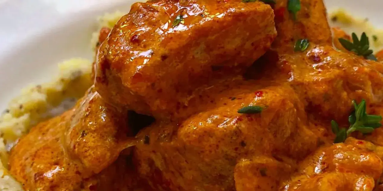 Sabroso pavo en salsa cremosa, adornado con hierbas frescas, servido sobre puré de patatas.