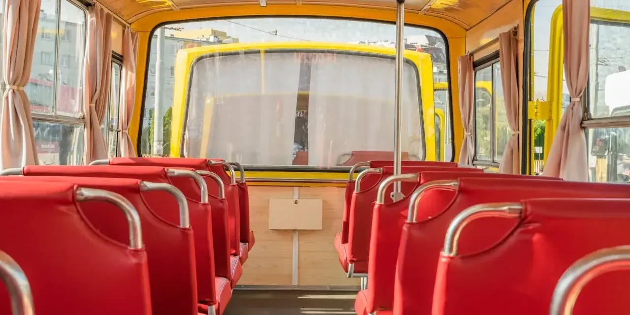Wnętrze żółtego autobusu z czerwonymi siedzeniami, widok od tyłu.