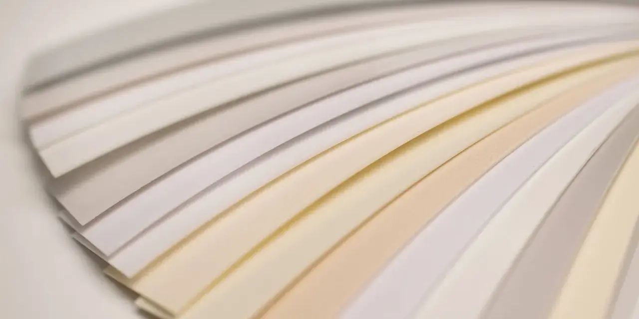 Próbki papieru ułożone wachlarzowo, ukazujące subtelne odcienie bieli i beżu.