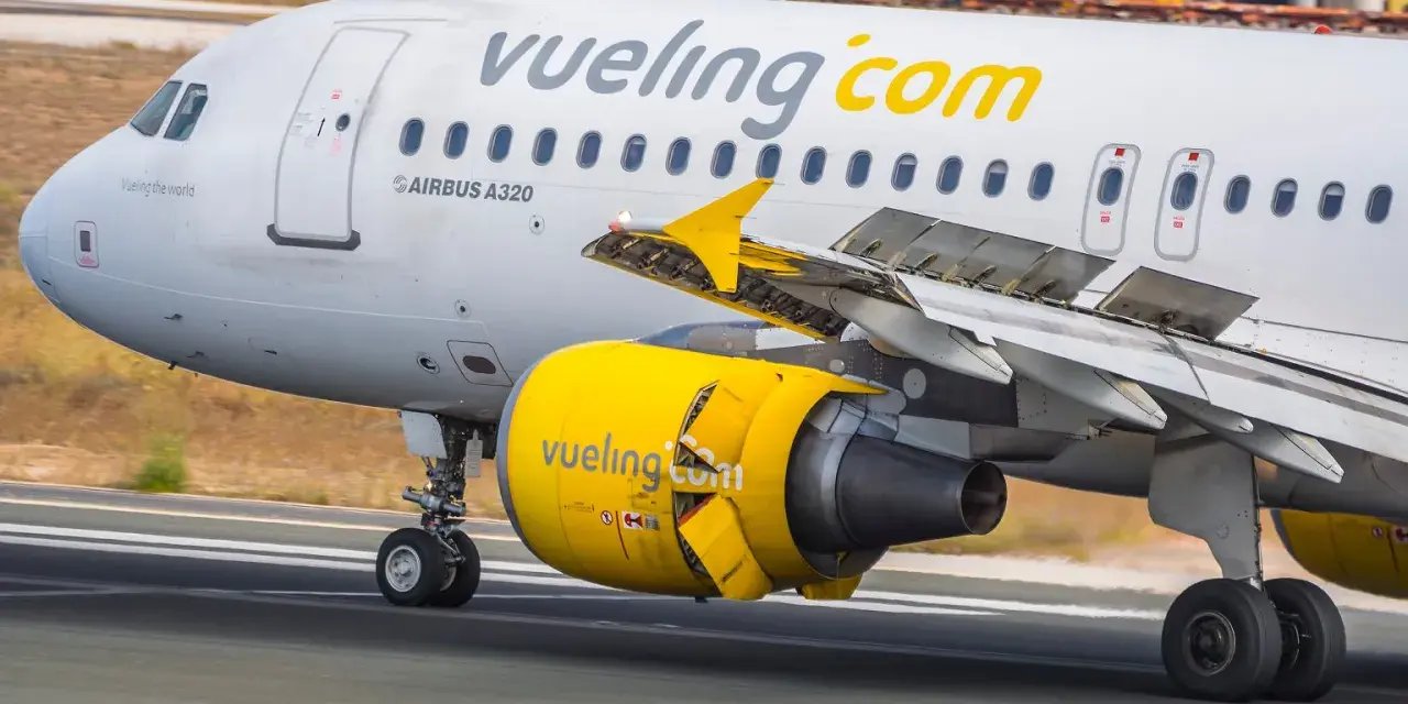 Samolot linii Vueling, hiszpańskie linie lotnicze, z żółtym silnikiem i logo na skrzydle, kołuje po pasie startowym.