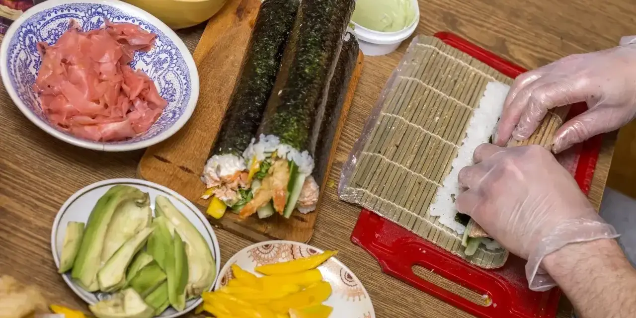 Przygotowanie domowego sushi: ryż, awokado, mango, imbir i rolki w trakcie zwijania.