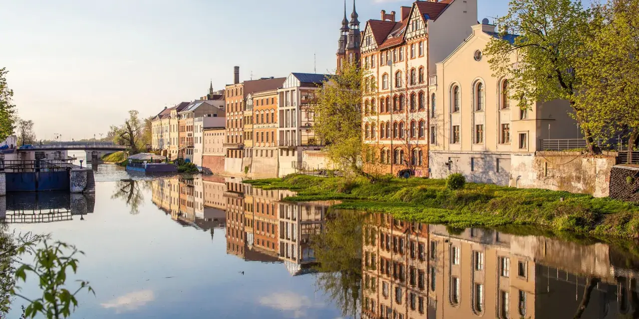 Nad Odrą w Opolu, zabytkowe kamienice odbijają się w wodzie. Spacerując brzegiem, odkryjesz urokliwe zakątki, co można zwiedzić w Opolu.