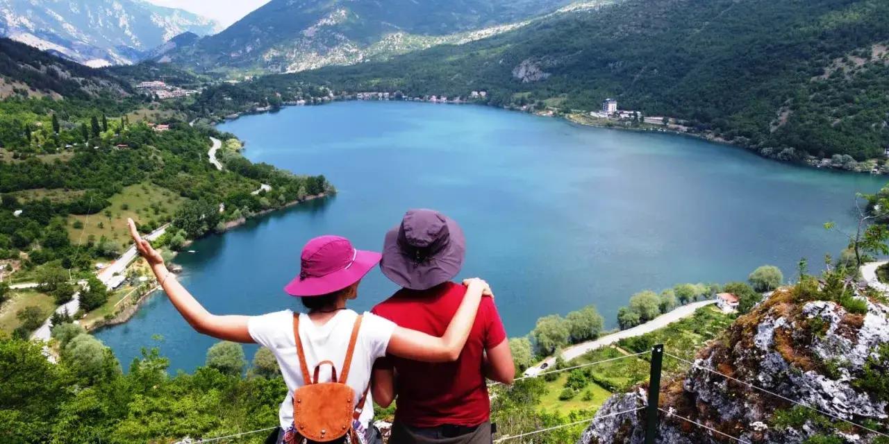 Coppia ammira un lago a forma di cuore, circondato da montagne verdi e alberi.