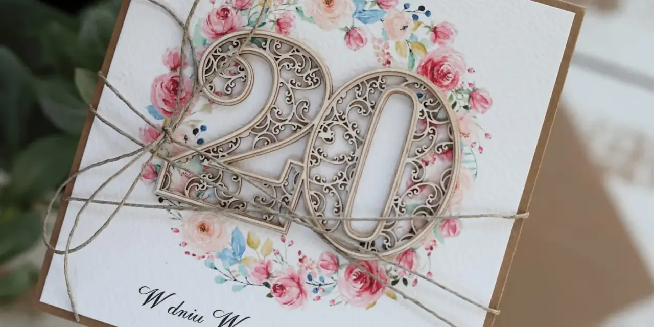 Elegancka kartka z życzeniami na 20 rocznicę ślubu, ozdobiona drewnianą cyfrą "20" i kwiatowym wiankiem.