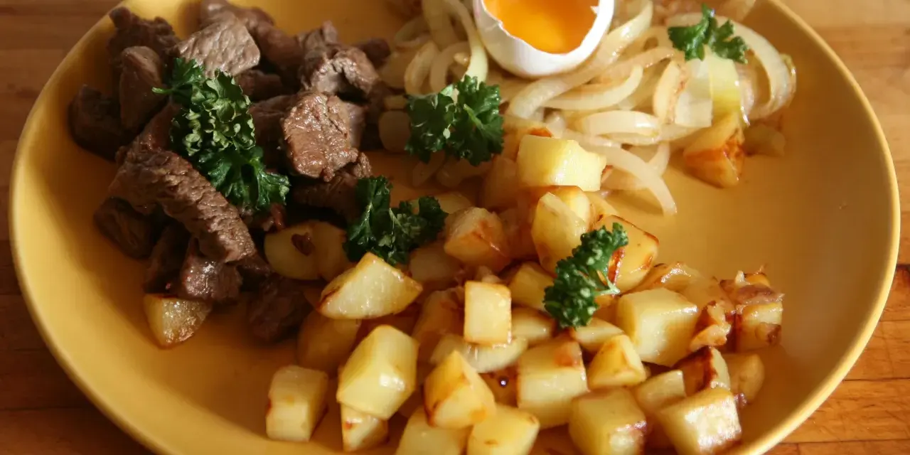 En tallrik med stekt kött, stekt potatis, stekt lök och ett kokt ägg. En klassisk rätt som representerar svenskt mat.