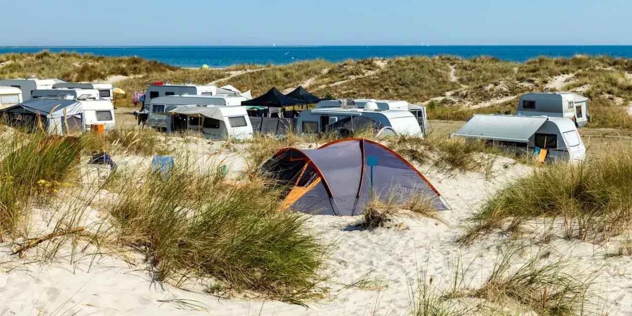 Ein sonniger Campingplatz in Deutschland am Meer. Wohnwagen und Zelte stehen zwischen Dünen und Strandhafer.