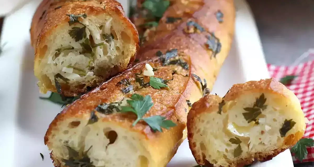 Pan de ajo recién horneado, dorado y crujiente, con trozos de perejil y ajo visibles en su interior.