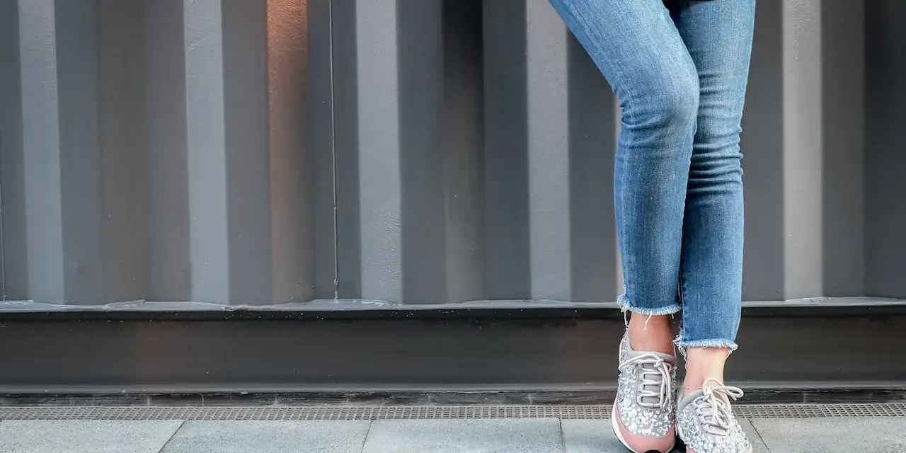 Nogawki jeansów postrzępione na dole, w połączeniu z błyszczącymi sneakersami, tworzą modny look.