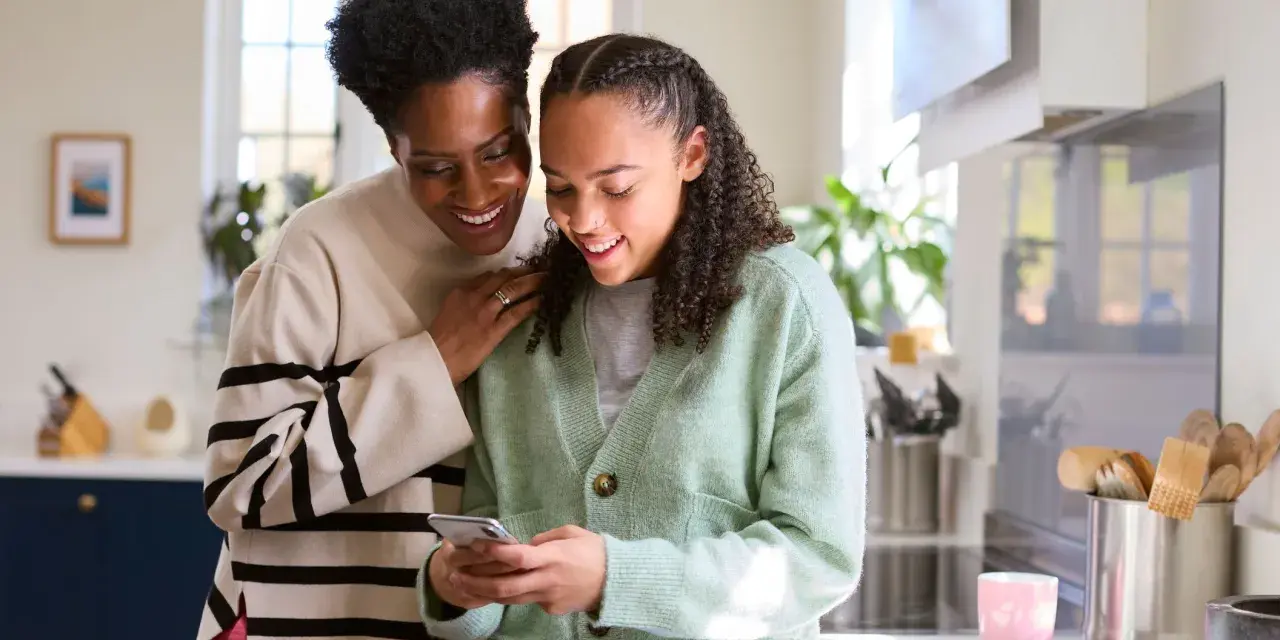 Mère et fille souriantes regardant un téléphone. Une conversation sur la pension alimentaire jusqu'à quel âge.