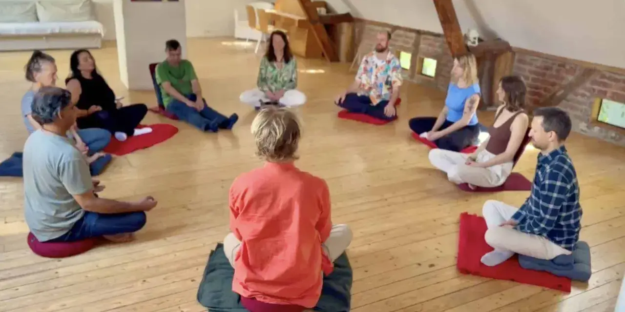 Menschen sitzen im Kreis auf Meditationskissen. Eine Gruppe genießt eine **Auszeit im Kloster**, umgeben von Ruhe und Gemeinschaft.