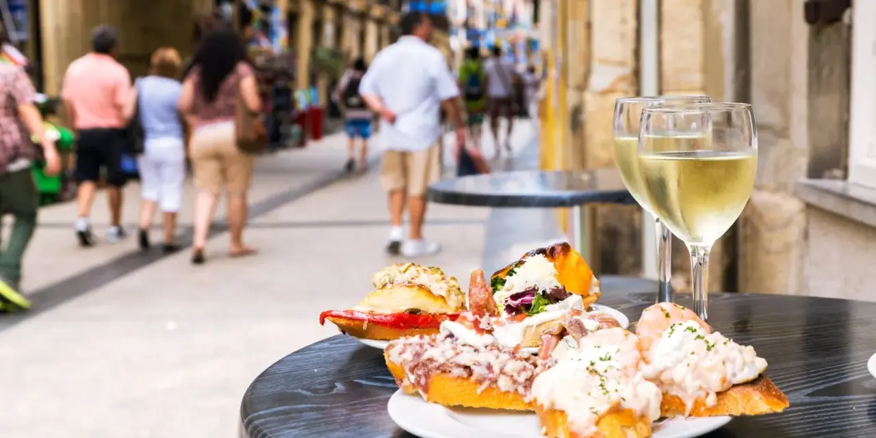 Njut av utsökt san sebastian mat och vitt vin på ett café. Folk promenerar på gatan i bakgrunden.