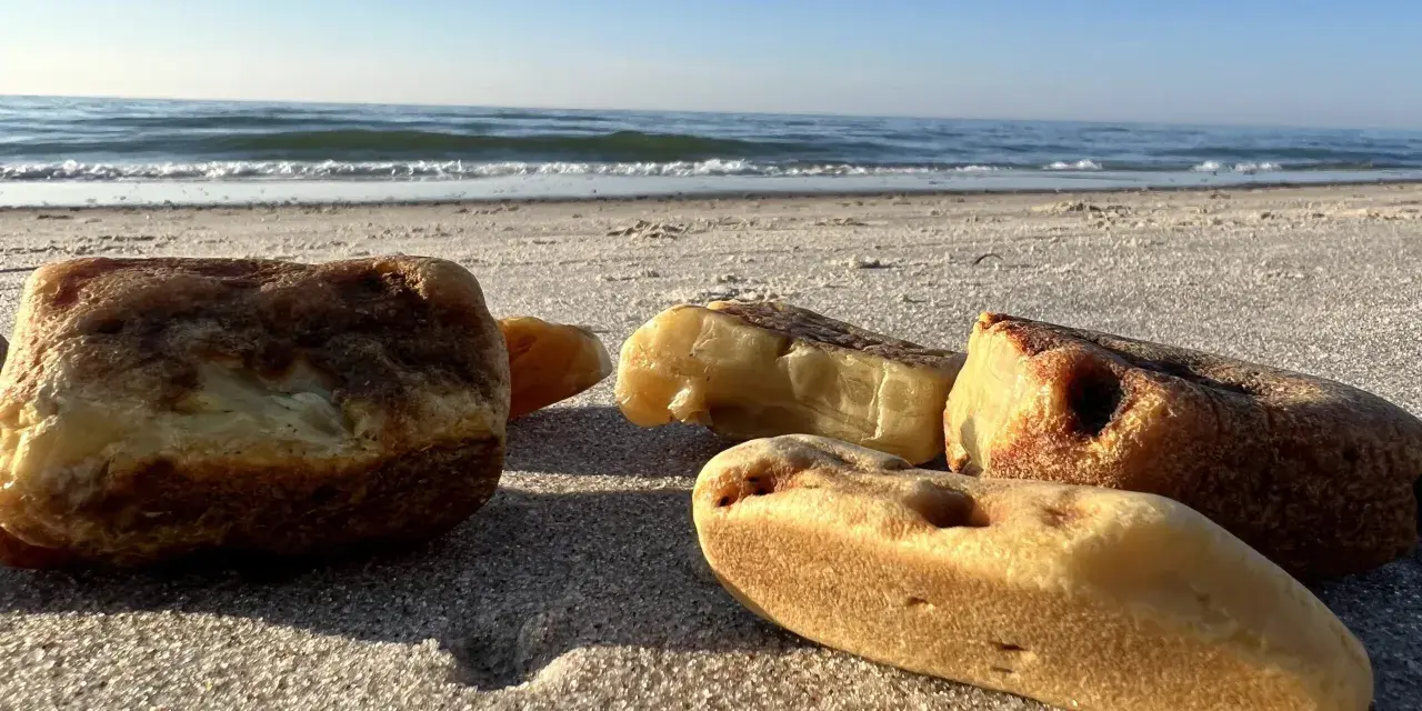 Kawałki bursztynu na piaszczystej plaży, z widokiem na spokojne morze i błękitne niebo.